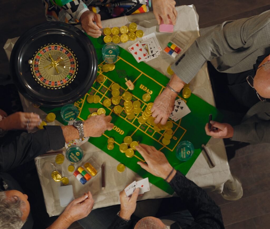 Overhead view of hands around a green roulette and craps layout piled with gold chips